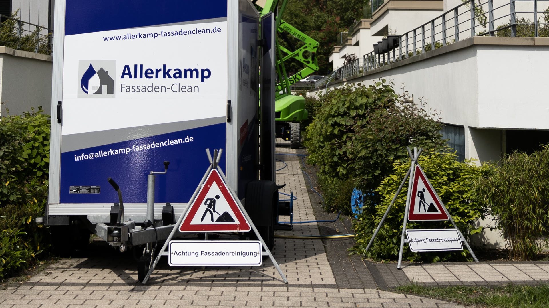 Der Anhänger mit der Aufbereitungsanlage und dem Firmenlogo steht an der Zufahrt eines Wohnobjekts, davor Warnschilder mit der Aufschrift Achtung Fassadenreinigung.