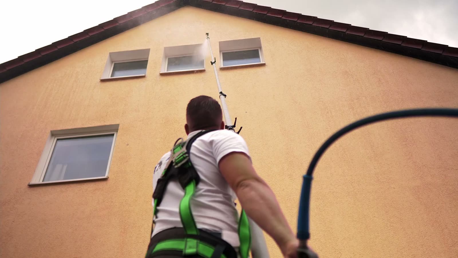 Mitarbeiter reinigt den Giebel eines Wohnhauses mit der Teleskoplanze, vom Boden aus, ohne Gerüst.