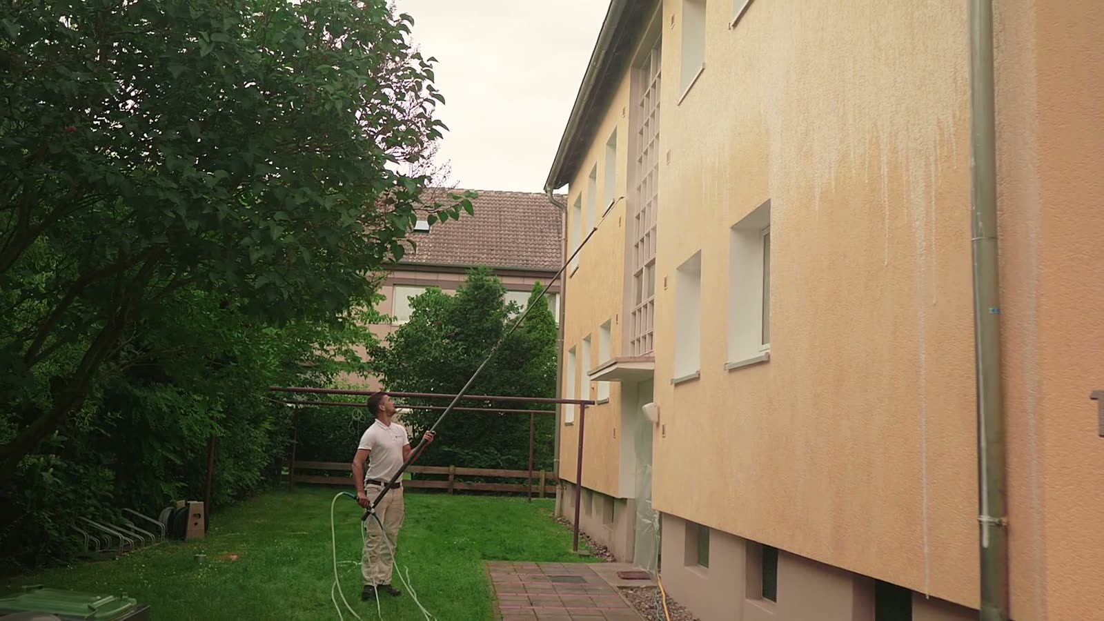 Reinigung der Fassade eines Mehrfamilienhauses vom Boden aus, Teleskoplanze reicht bis unters Dach.