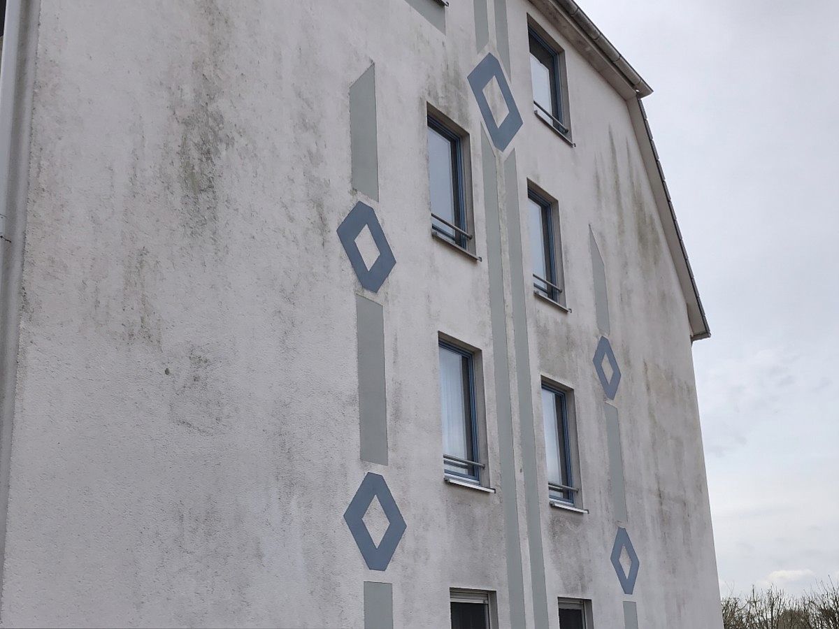 Mehrfamilienhaus mit vergrauter Giebelwand, vor der Reinigung.