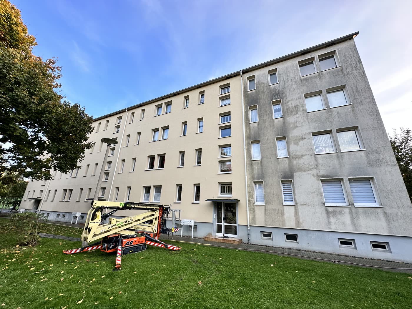Giebelseite einer Wohnanlage mit flächigen dunklen Ablaufspuren, davor die Arbeitsbühne, vor der Reinigung.