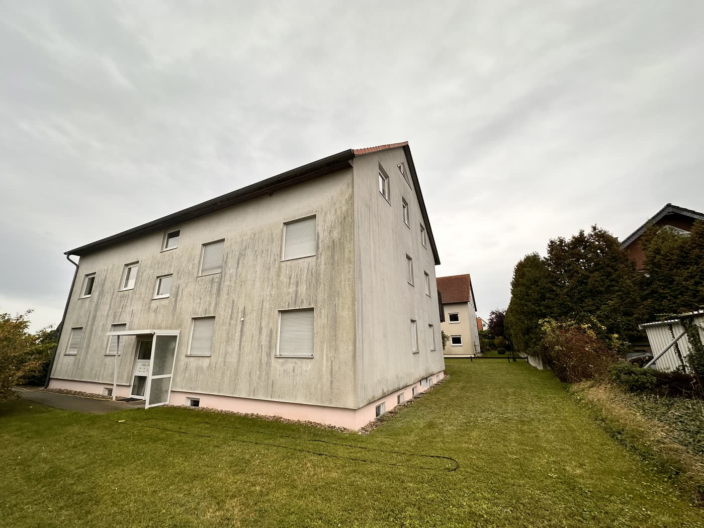 Mehrfamilienhaus mit Satteldach, die Giebelwand von dunklen Ablaufspuren durchzogen, vor der Reinigung.
